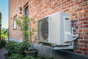 Side view of outdoor energy unit hanging on brick wall of beautiful house on a sunny day. Air conditioner or air heat pump. Outdoor unit powered by renewable energy. CREDIT: iStock/NAPA74